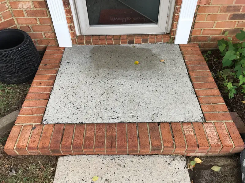 A concrete landing framed in red brick at a front door, part way through a wash