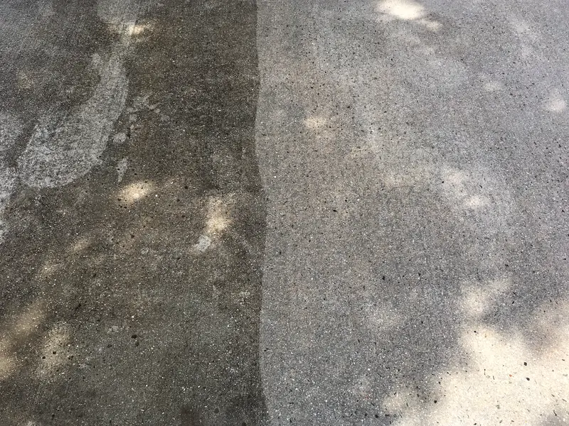 A concrete driveway in the middle of a wash: grey and stained on the left, clean on the right, a straight edge between