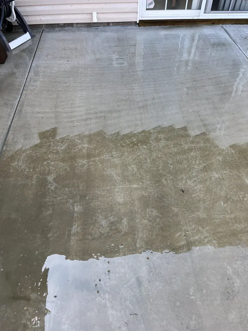 A concrete patio half washed, a stepped clean edge across it
