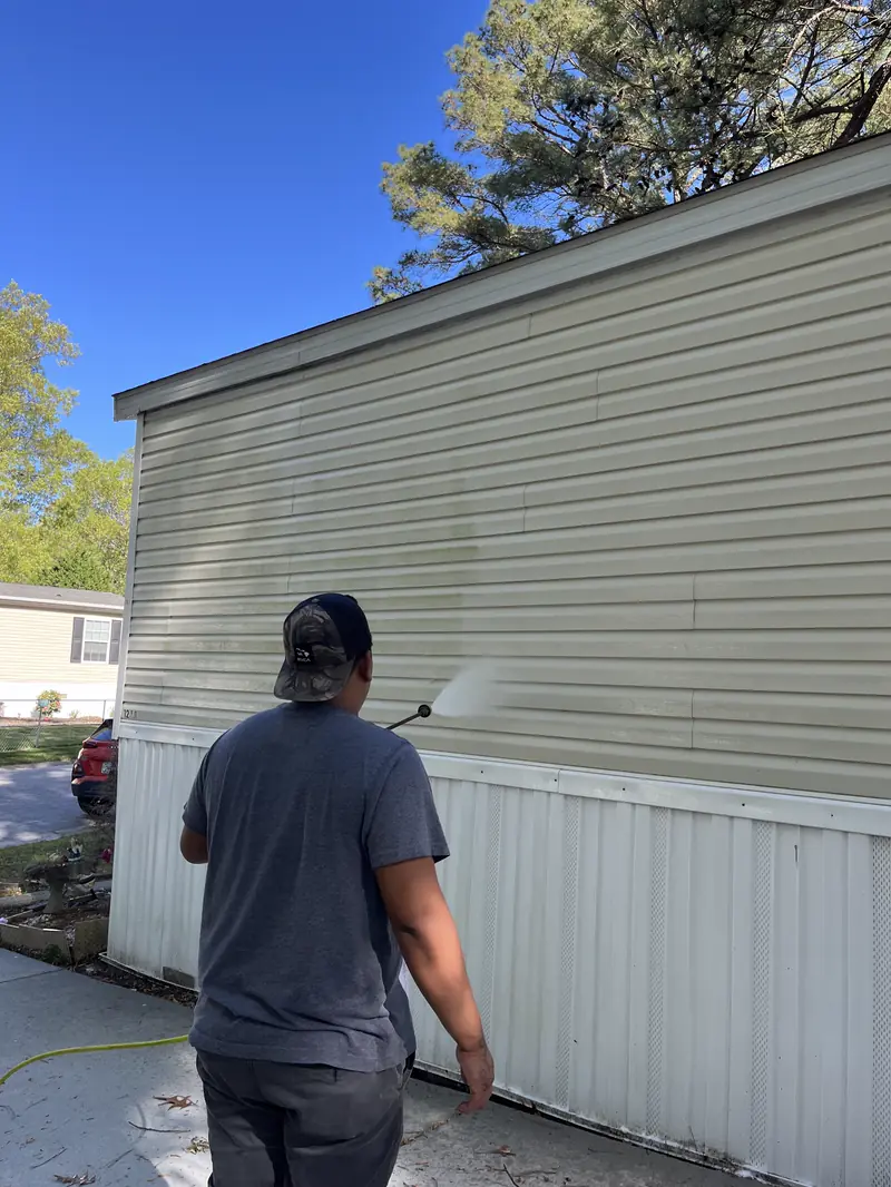 Robert, seen from behind, washing pale yellow vinyl siding with a pressure wand